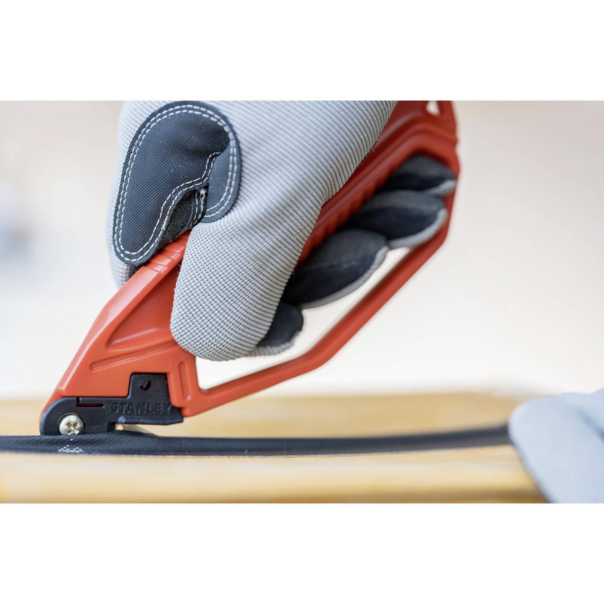 Dłoń w wyściełanej rękawicy trzyma czerwony nóż krążkowy i ostrożnie przecina czarną tkaninę.