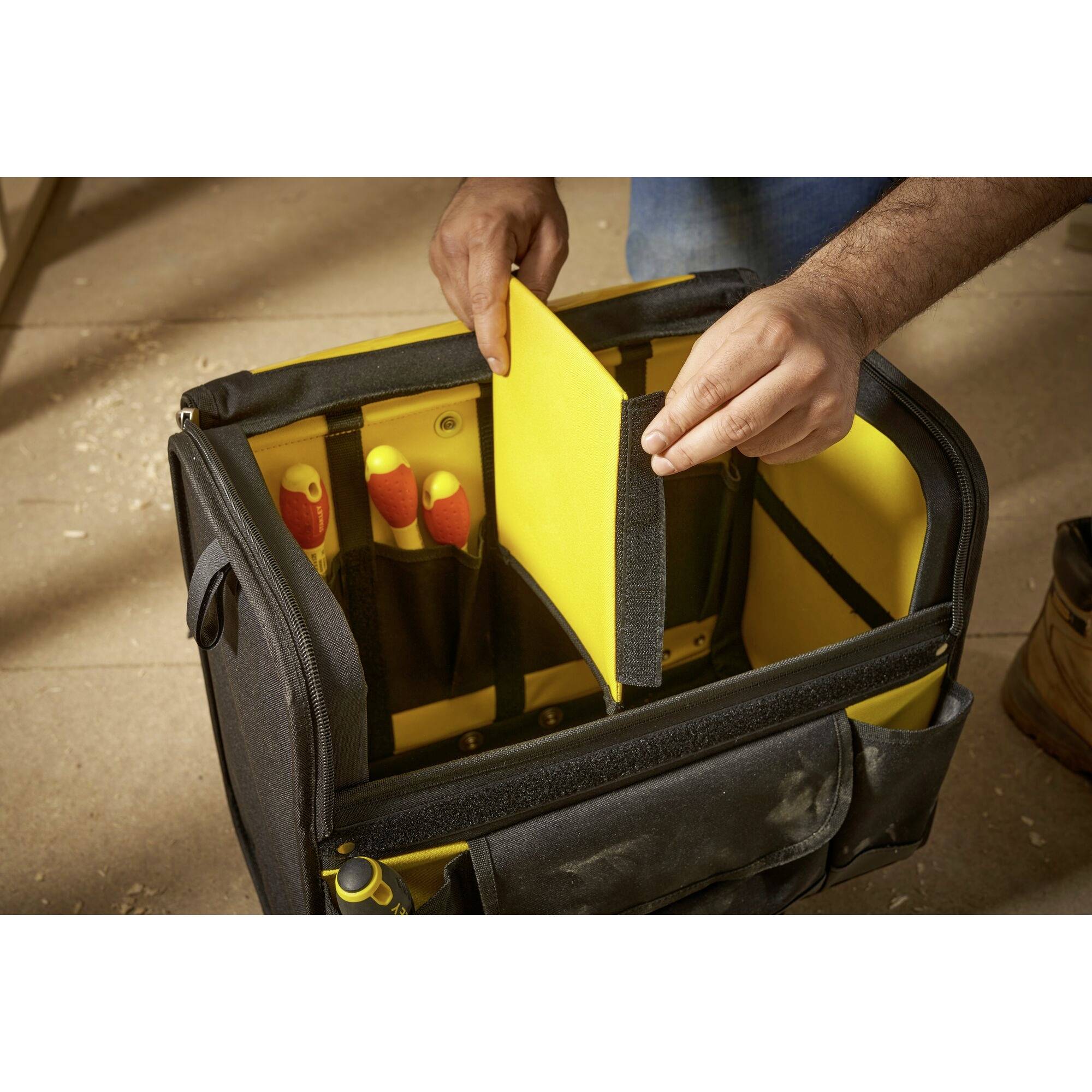Osoba organizuje narzędzia w otwartej torbie narzędziowej z żółtymi przegródkami. Widoczne są wkrętaki i szczypce.