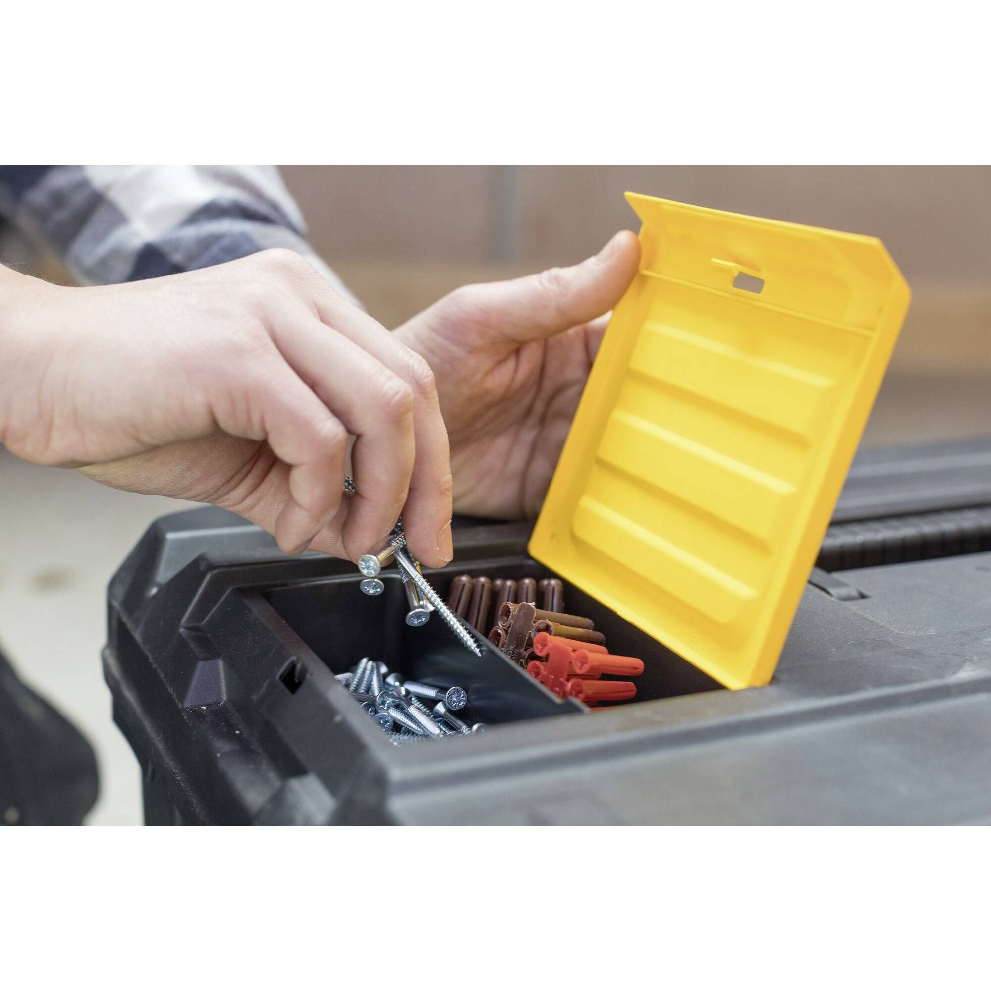 Osoba sortuje śruby i kołki w żółtym pojemniku na skrzynce narzędziowej. Ręce na pierwszym planie, nacisk na organizację.