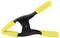 Czarna plastikowa klamra z żółtymi uchwytami w pozycji zamkniętej; służy do przytrzymywania przedmiotów podczas pracy.