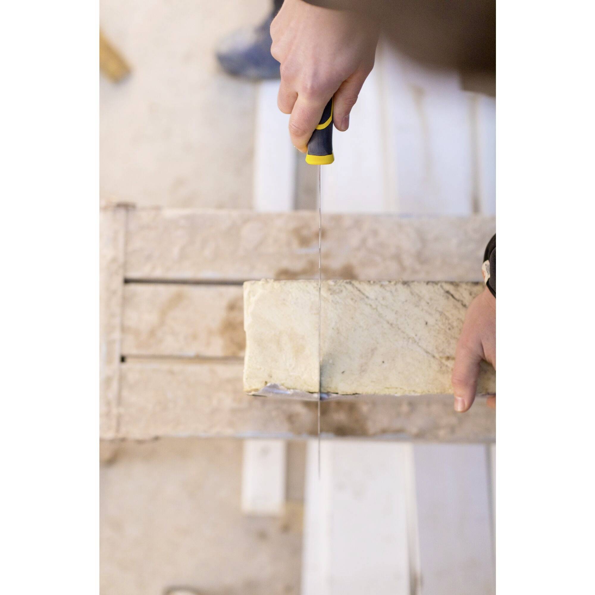 Człowiek piłuje prostokątny blok kamienny ręczną piłą na drewnianym stole.