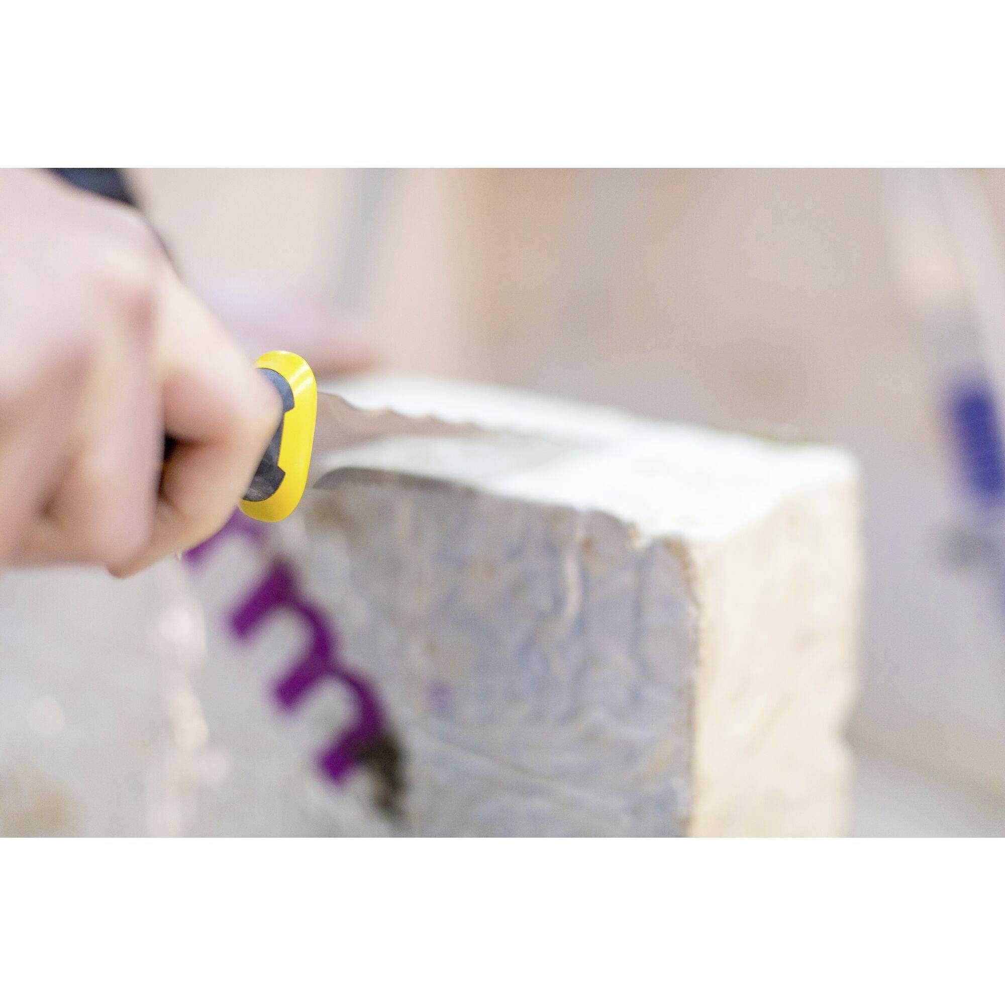 Osoba przecina kawałek materiału izolacyjnego żółtym nożem. Ruch wskazuje na precyzyjną robotę ręczną.