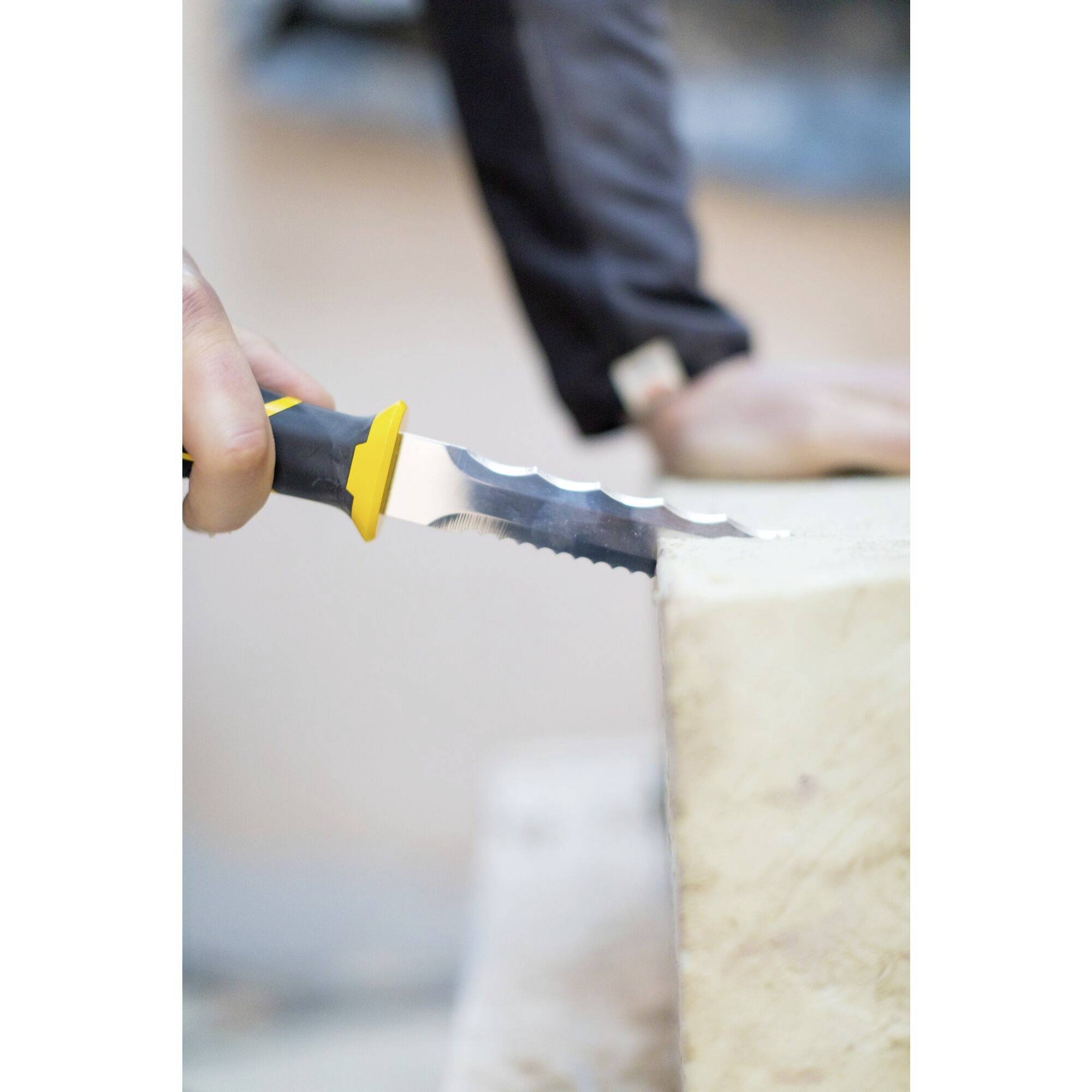 Dłoń przyciska ząbkowany nóż w bloku, z ostrym skupieniem na ostrzu.