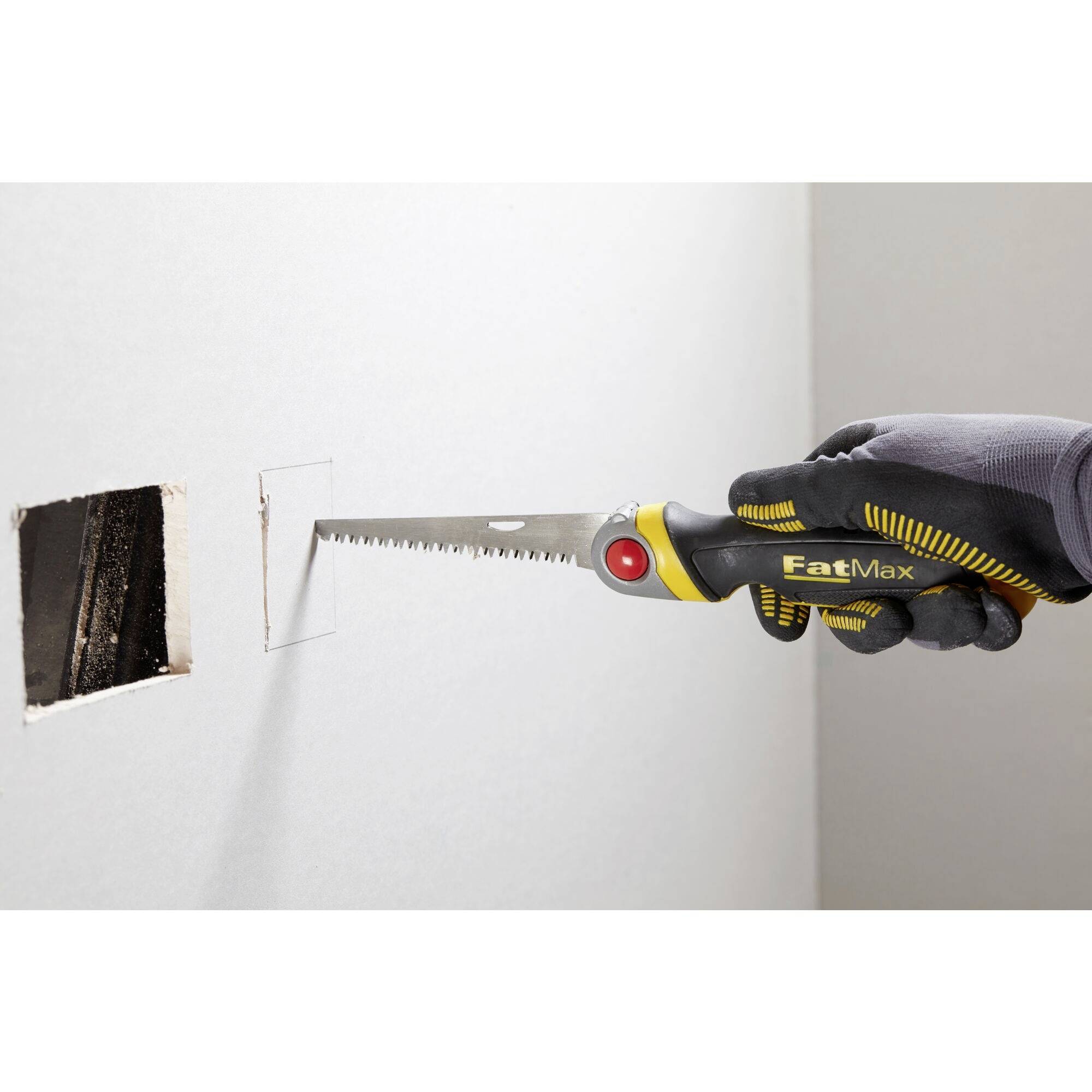 Ręka podcina piłą ręczną kwadratowy otwór w ścianie. Piła ma żółtą rękojeść z czerwonym wkładem.
