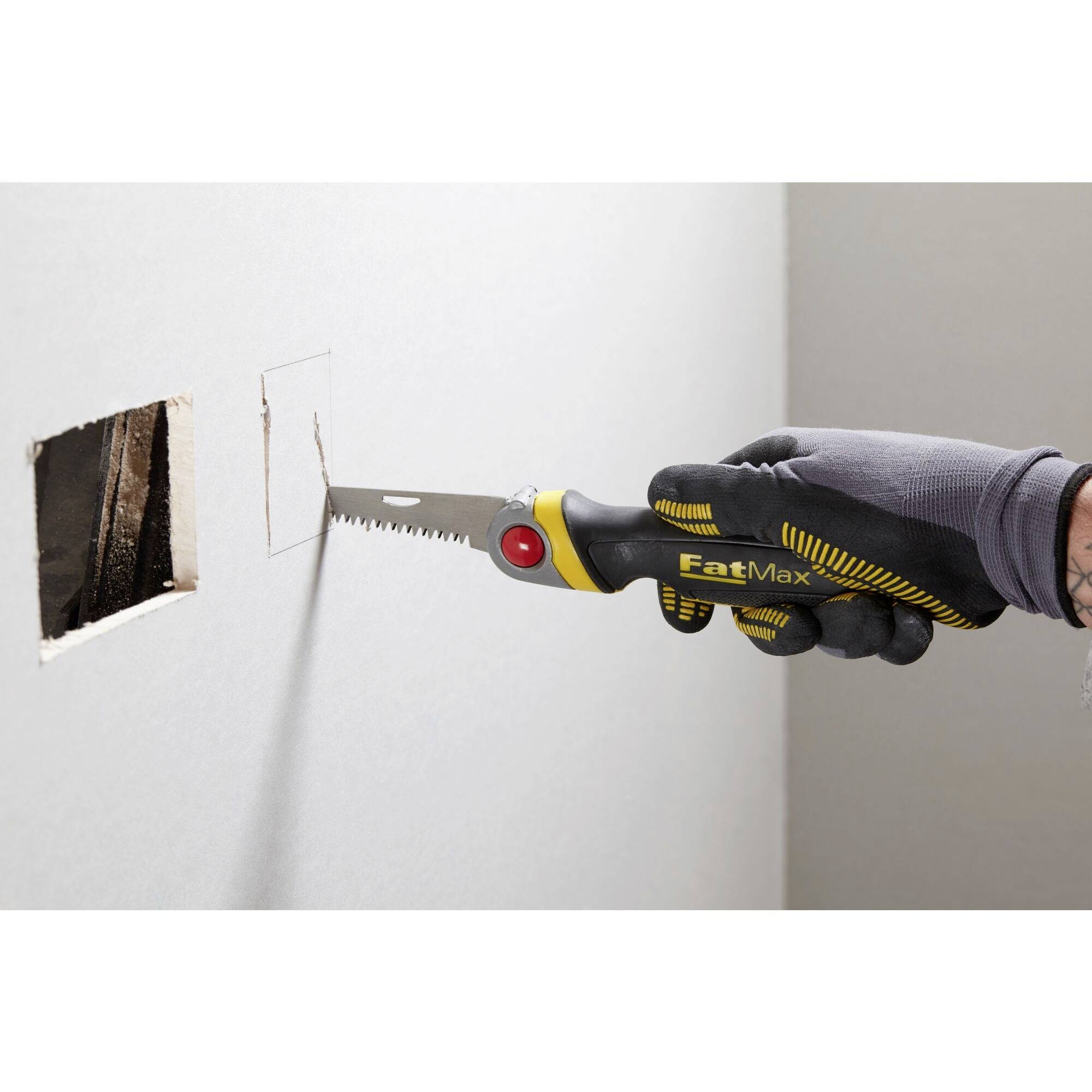 Osoba w rękawicach wycina prostokątny otwór w ścianie z płyty gipsowo-kartonowej za pomocą piły.