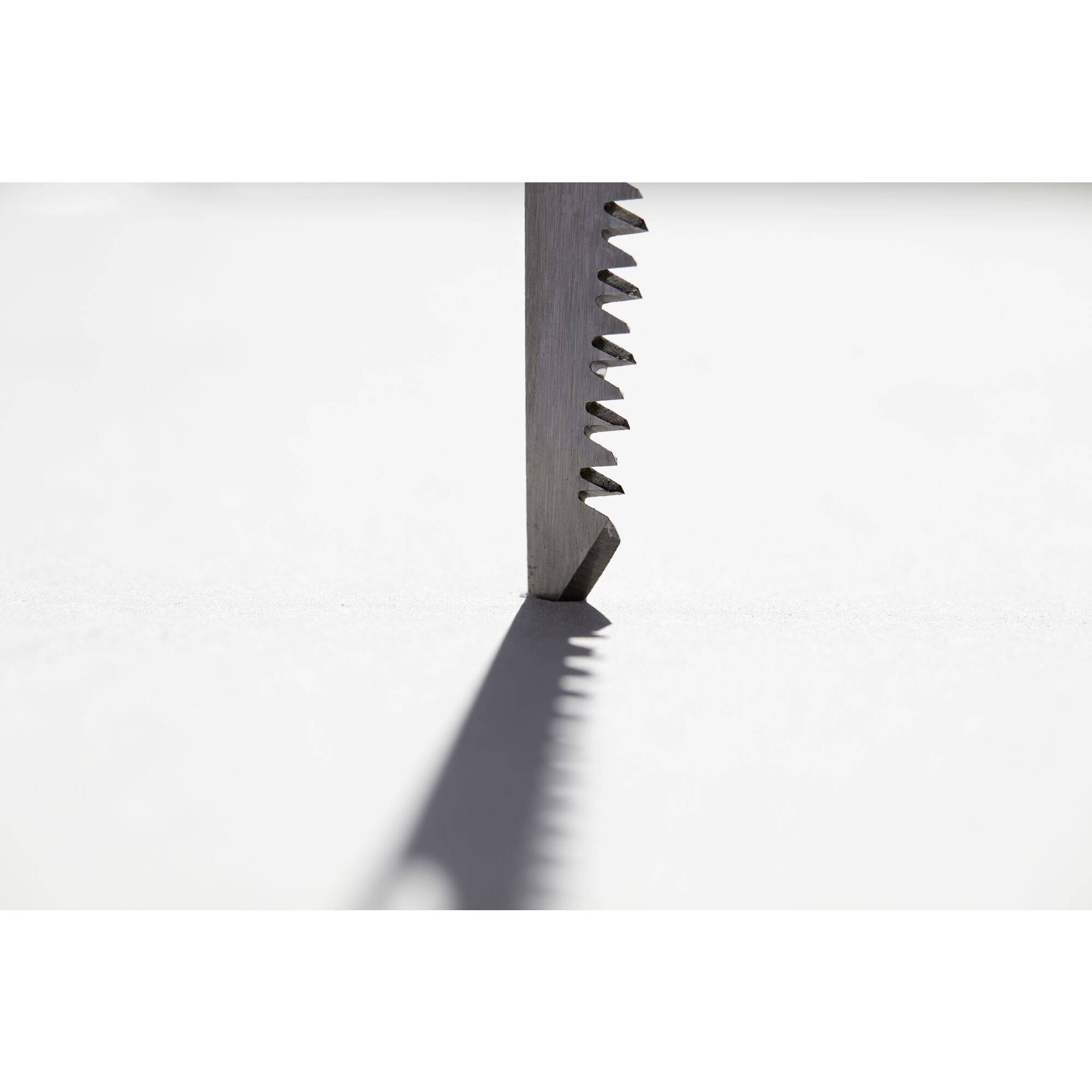 Zbliżenie czubka piły, ustawionej pionowo, z zębami rzucającymi cień na gładką białą powierzchnię.