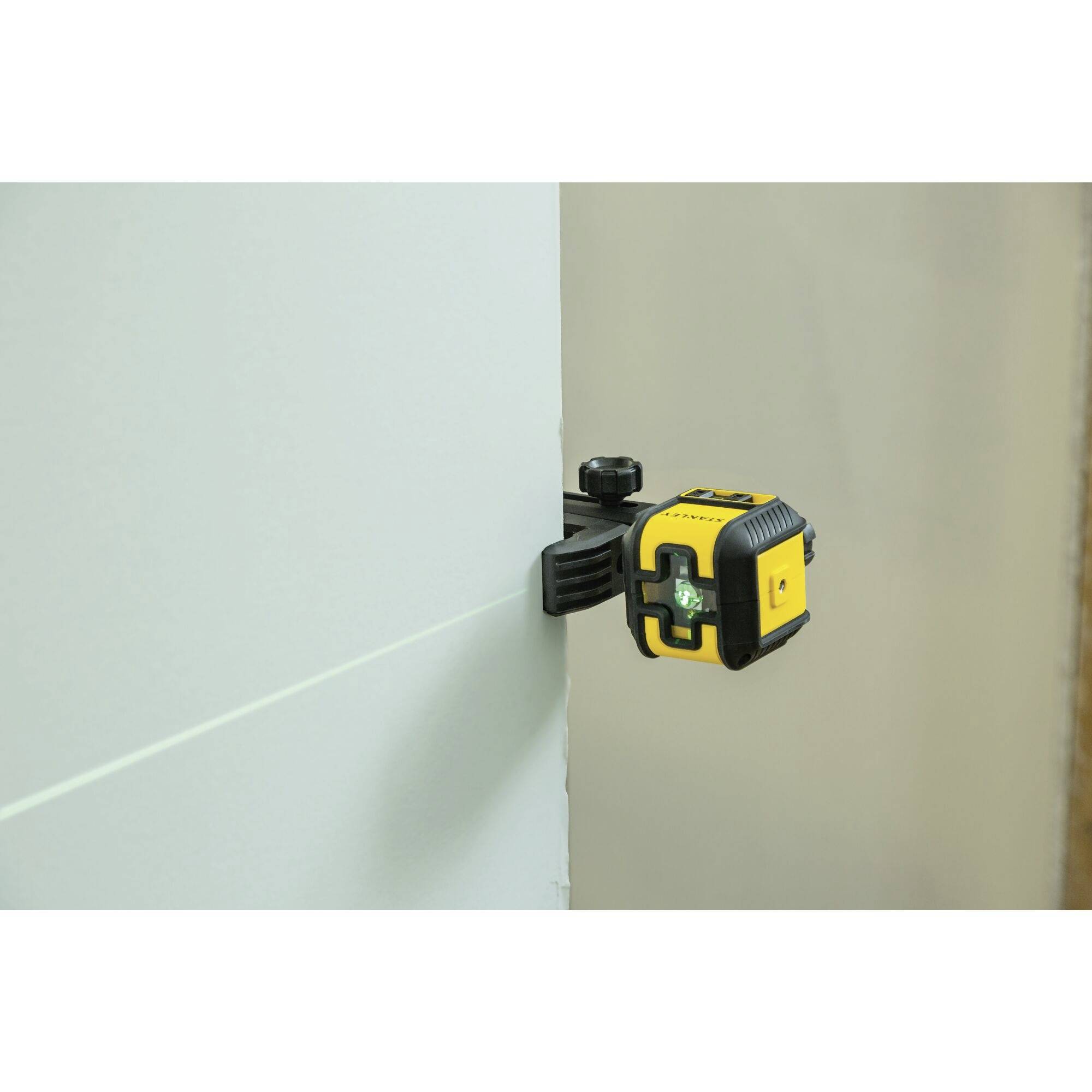 Żółto-czarny laser poziomujący jest zamocowany na ścienie i rzutuje poziomą zieloną linię.