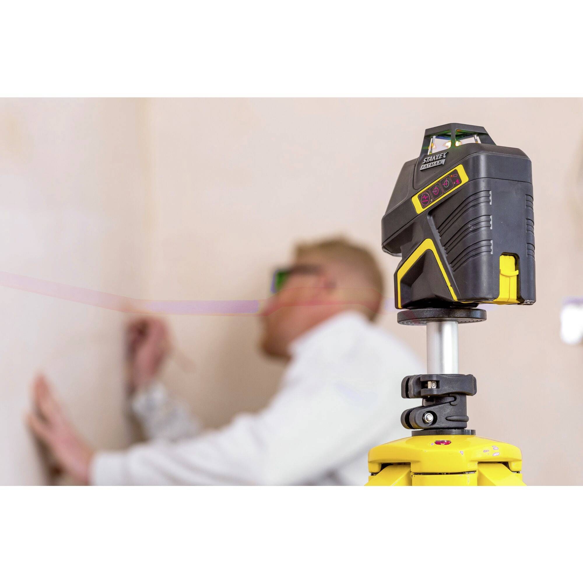 Robotnik budowlany wyrównuje ścianę za pomocą żółtego laserowego urządzenia pomiarowego. Urządzenie służy do dokładnych pomiarów.