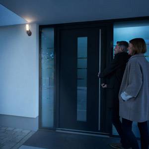 Para stoi wieczorem przed nowoczesnym wejściem do domu, oświetlonym latarnią, drzwi są zamknięte.