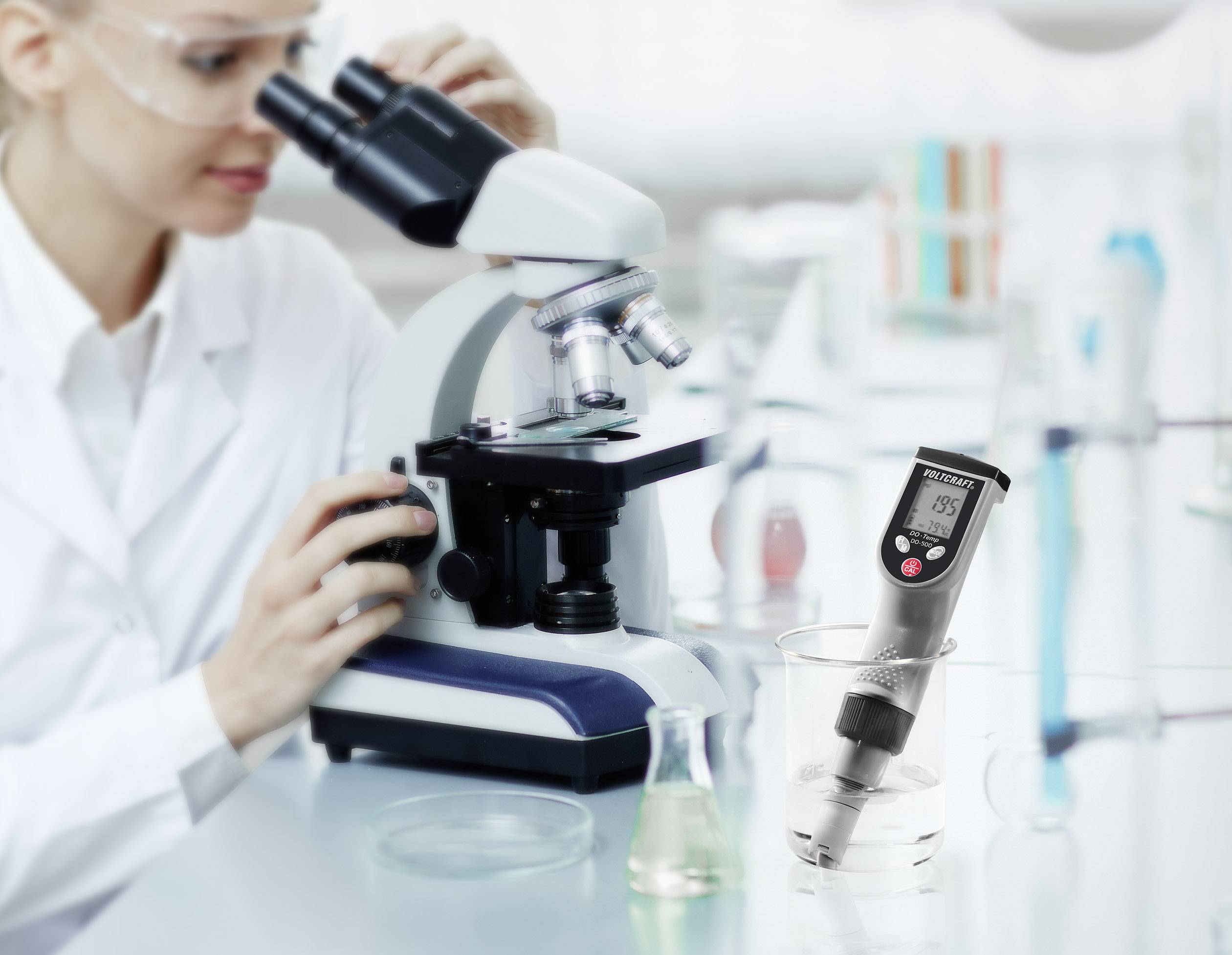 Naukowiec przygląda się próbce przez mikroskop. Cyfrowy pH-metr mierzy poziom pH płynu obok niej.