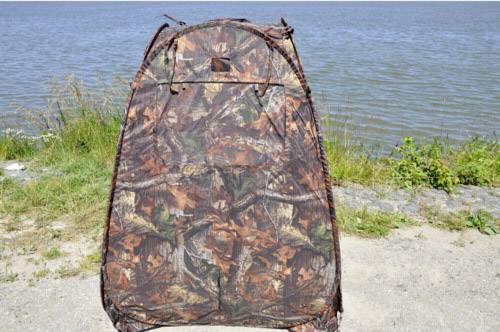 Namiot maskujący stoi nad brzegiem akwenu. Namiot posiada wzór z liści i gałęzi, który jest dopasowany do otoczenia.