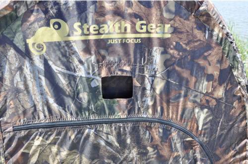 Namiot maskujący 'Stealth Gear' z napisem 'Just Focus', w kamuflażu, z zamkniętym oknem widokowym i zamkiem błyskawicznym.