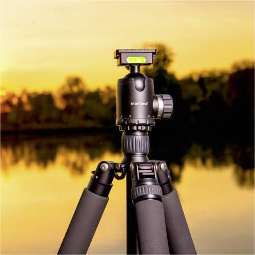 Statyw stoi nad brzegiem jeziora podczas zachodu słońca. Niebo jest zabarwione na pomarańczowo, a drzewa odbijają się w wodzie.