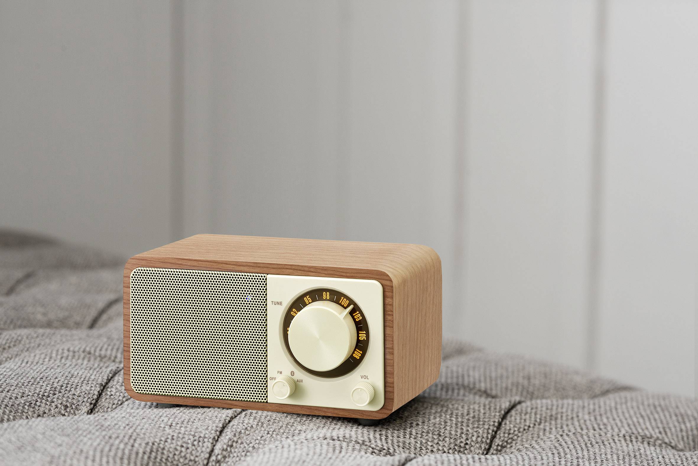 Zabytkowe radio z drewna z obrotowym pokrętłem i głośnikiem stoi na szarej powierzchni przed neutralną ścianą.