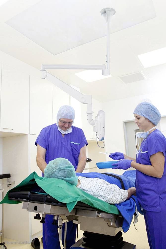 Pacjent leży na stole operacyjnym, podczas gdy dwóch chirurgów w niebieskich fartuchach i czepkach chirurgicznych przygotowuje się do zabiegu w sali operacyjnej.