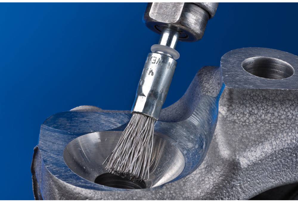 Druciana szczotka czyści wnętrze metalowego otworu w elemencie maszyny.