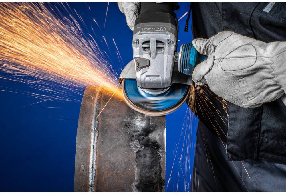Osoba szlifuje metalowy cylinder szlifierką kątową, z której lecą iskry. Osoba jest ubrana w odzież ochronną.