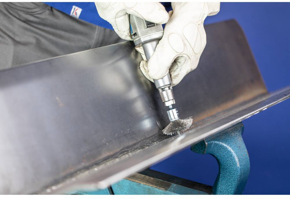 Robotnik w rękawicach poleruje krawędź metalową szlifierką kątową.