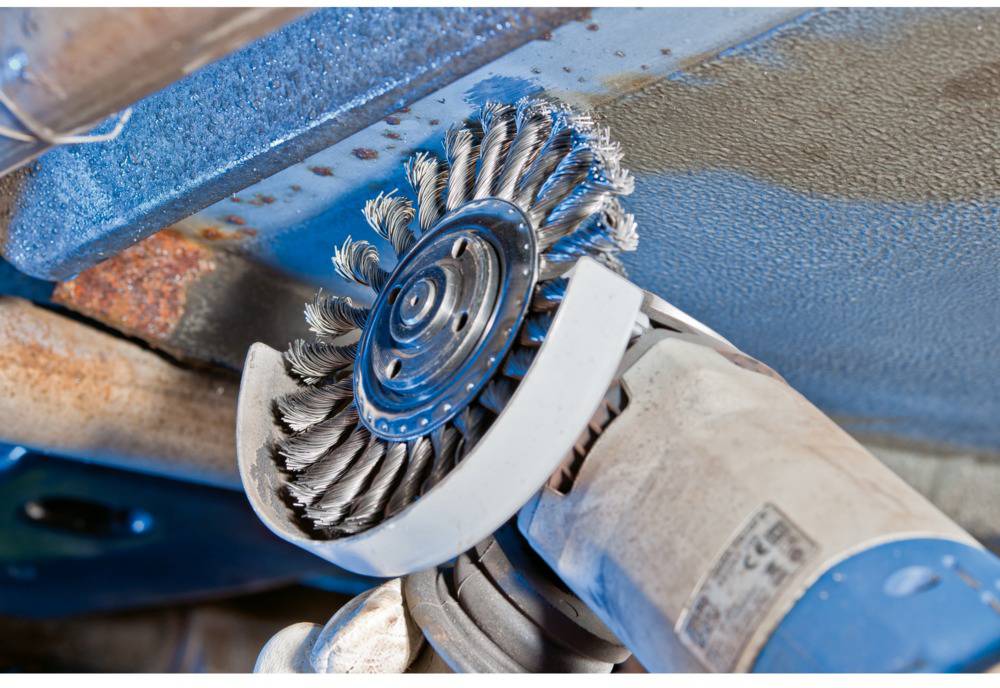 Szczotka druciana usuwająca rdzę z powierzchni metalowych. Zbliżenie pokazuje obracającą się szczotkę podczas pracy pod pojazdem.