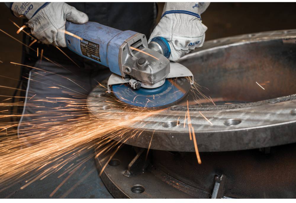 Osoba w rękawicach ochronnych szlifuje metal szlifierką kątową, a wokół tryskają iskry.