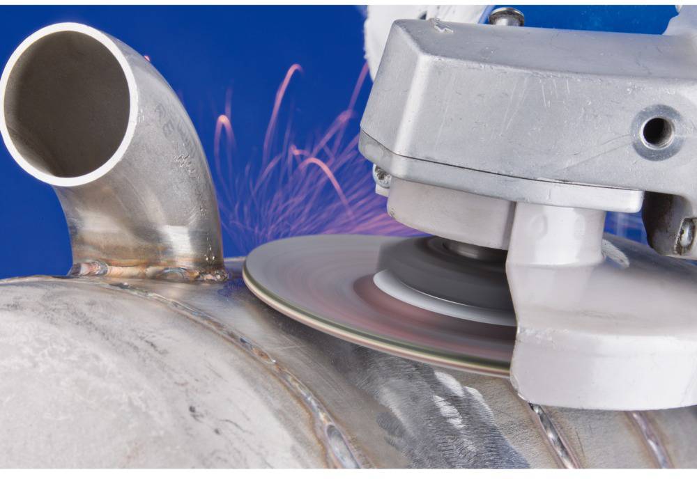 Szlifierka obrabia powierzchnię metalową, przy czym tryskają iskry. Scena przedstawia zbliżenie procesu szlifowania.