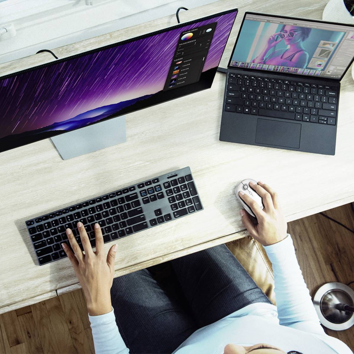 Widok z góry biurka z dwoma monitorami i laptopem. Osoba korzysta z komputerowej myszki. Na ekranie wyświetlony jest program do edycji zdjęć.