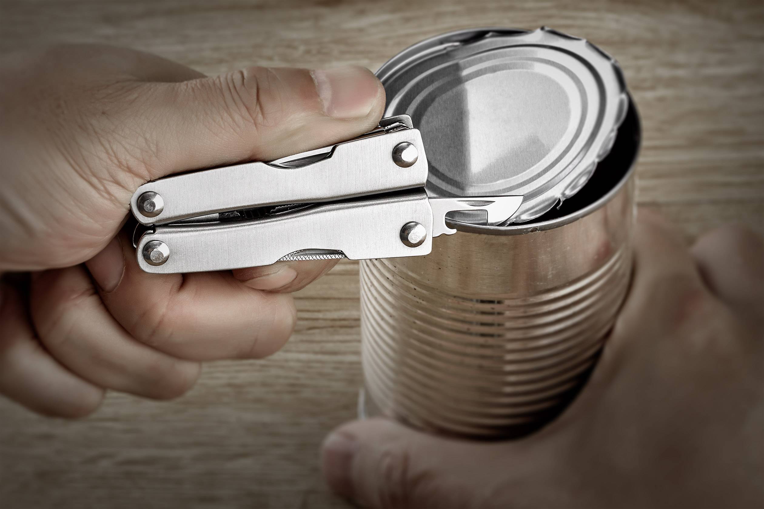 Osoba otwiera puszkę metalową za pomocą wielofunkcyjnego narzędzia.