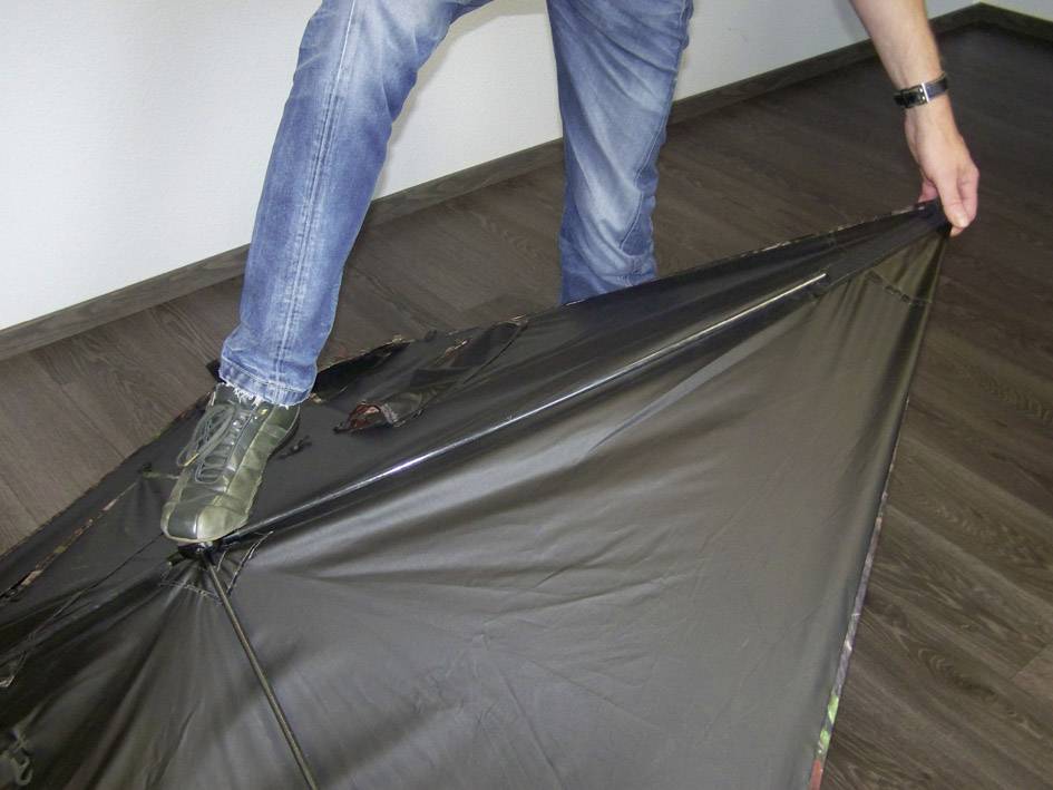 Osoba naciska butem na duży, czarny parasol, który leży na ziemi.