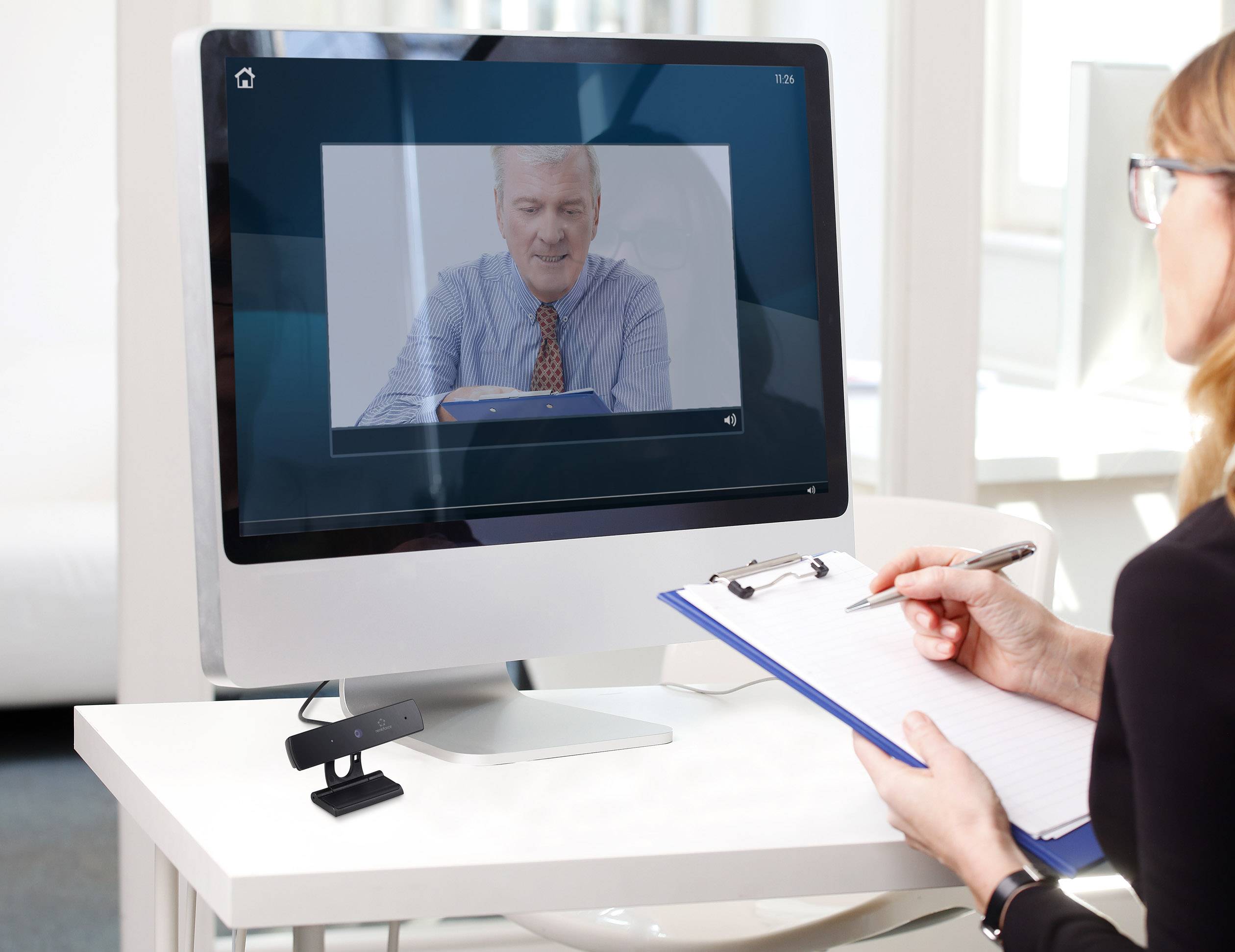 Kobieta sporządza notatki, oglądając wideo ze starszą osobą na ekranie komputera.