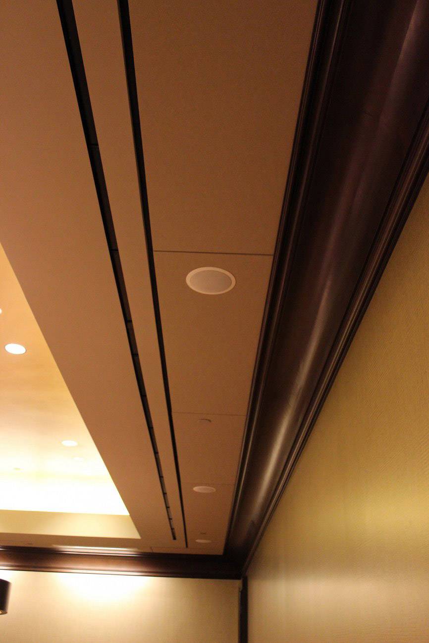 Podwieszany sufit z zintegrowanymi okrągłymi głośnikami i oświetleniem w korytarzu lub pomieszczeniu, elegancki design z drewnianymi akcentami.