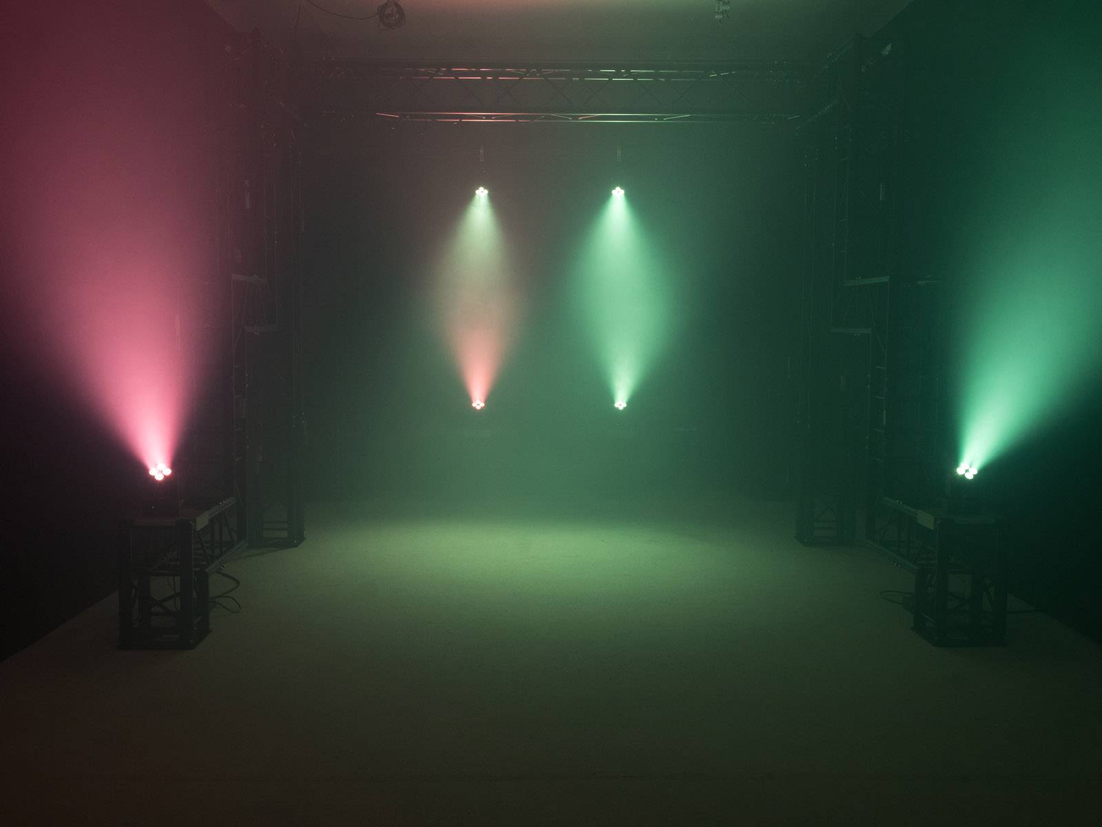 Scena z kolorowym oświetleniem: dwa czerwone i dwa zielone reflektory, które wytwarzają kolorowy dym w ciemnym pomieszczeniu.
