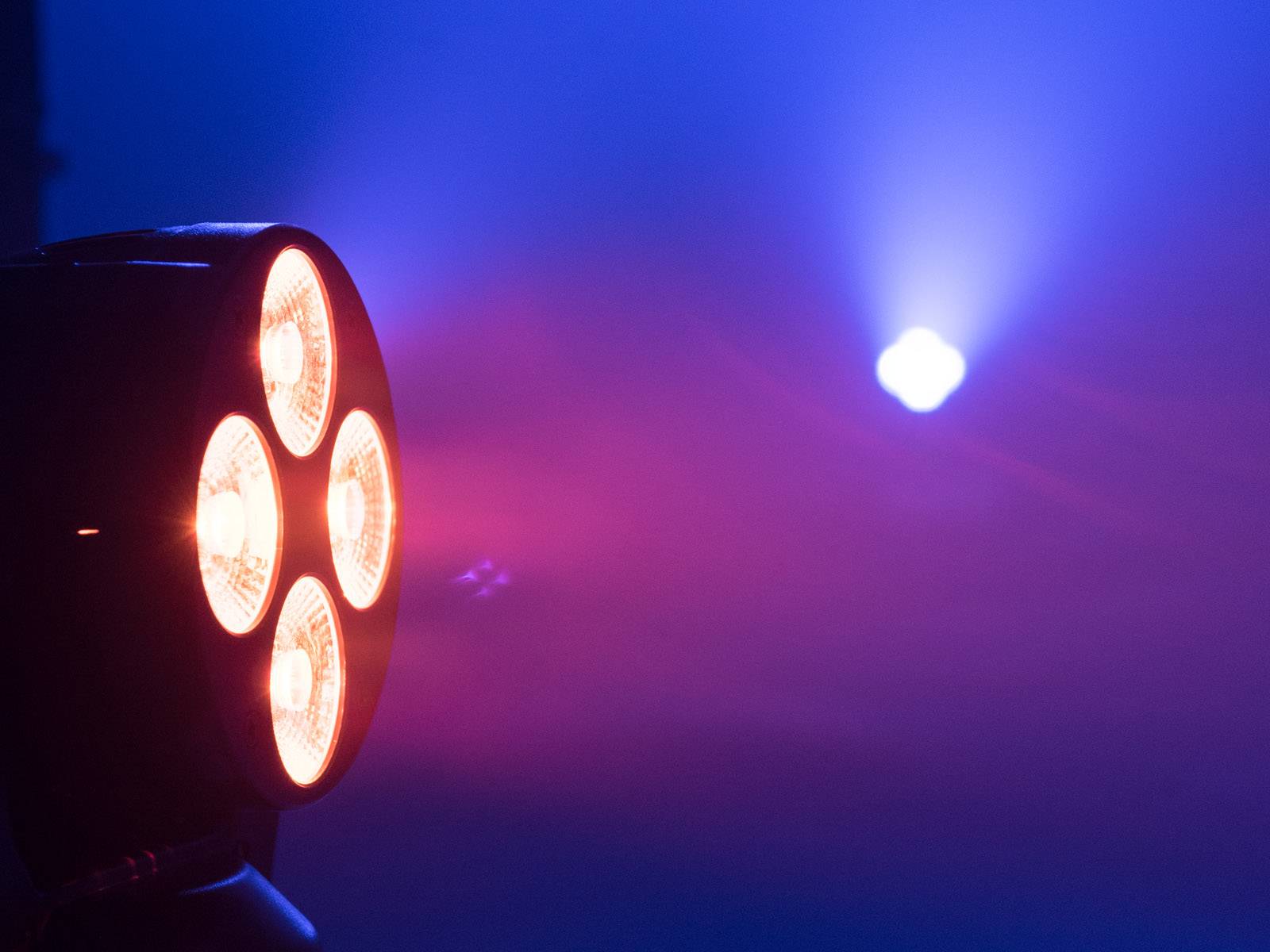 Czerwone światło sceniczne świeci w kierunku kamery, podczas gdy w tle niebieski snop światła biegnie ku górze.