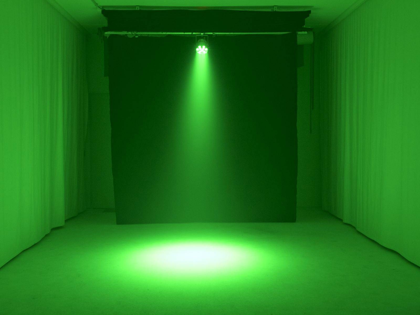 Ciemnozielone pomieszczenie z jasnym, zielonym reflektorem, który oświetla koło na podłodze.