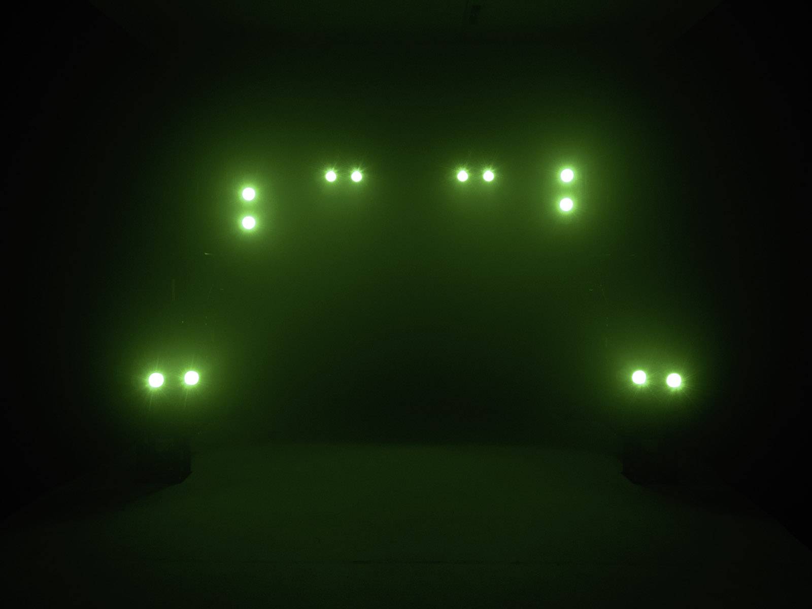 Ciemne pomieszczenie z wieloma zielonymi światłami ułożonymi parami. Światła tworzą symetryczny wzór.
