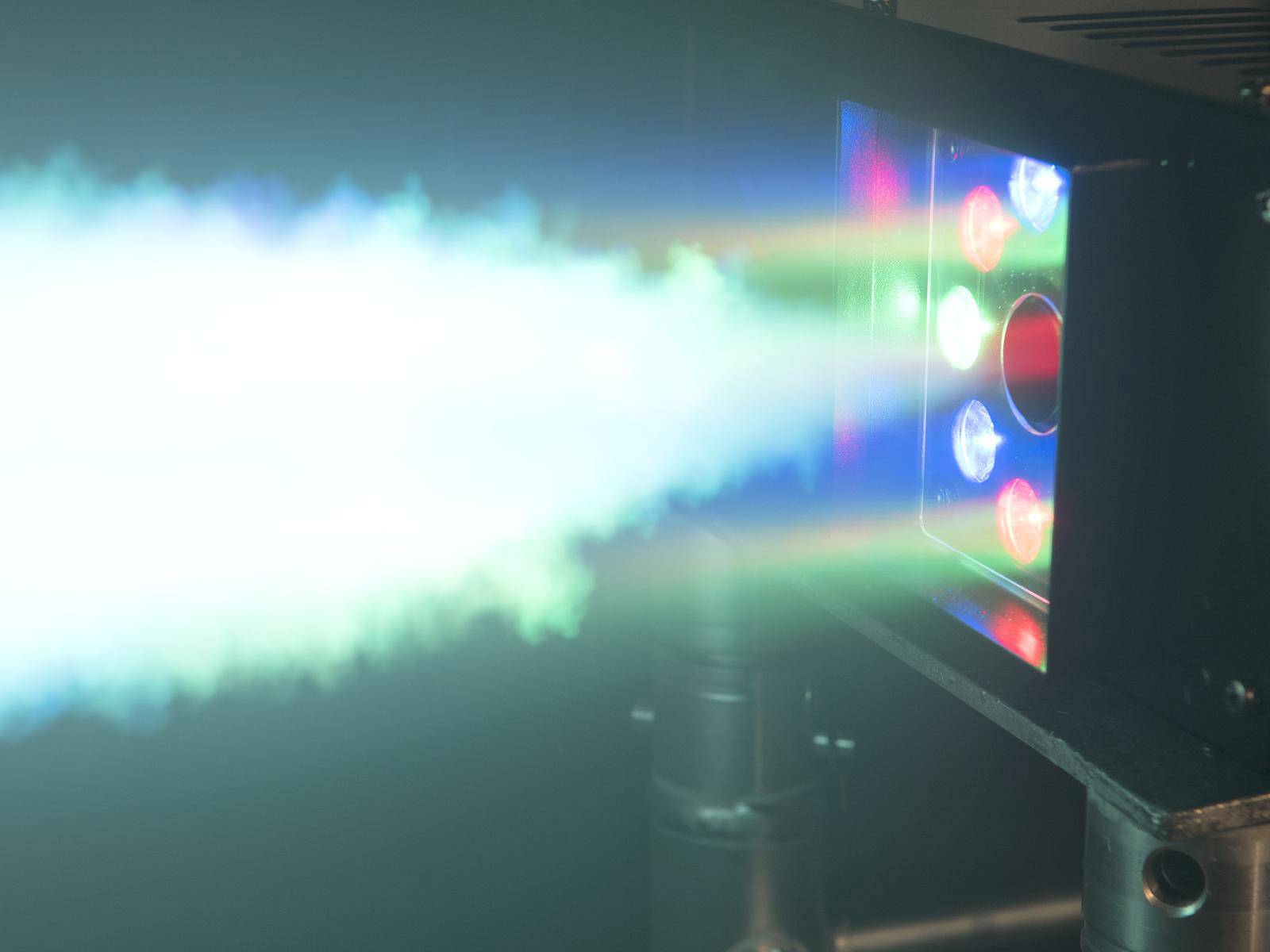 Projektor laserowy z kolorowymi wiązkami światła w ciemnym pomieszczeniu. Wyraźnie widoczne są emitowane wiązki zielonego, niebieskiego i czerwonego światła.