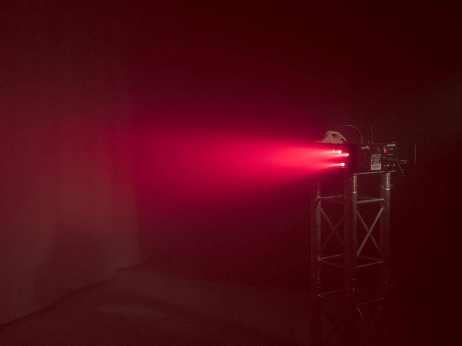 Czerwony promień laserowy jest emitowany przez projektor zamontowany na metalowej podstawie w ciemnym pomieszczeniu.