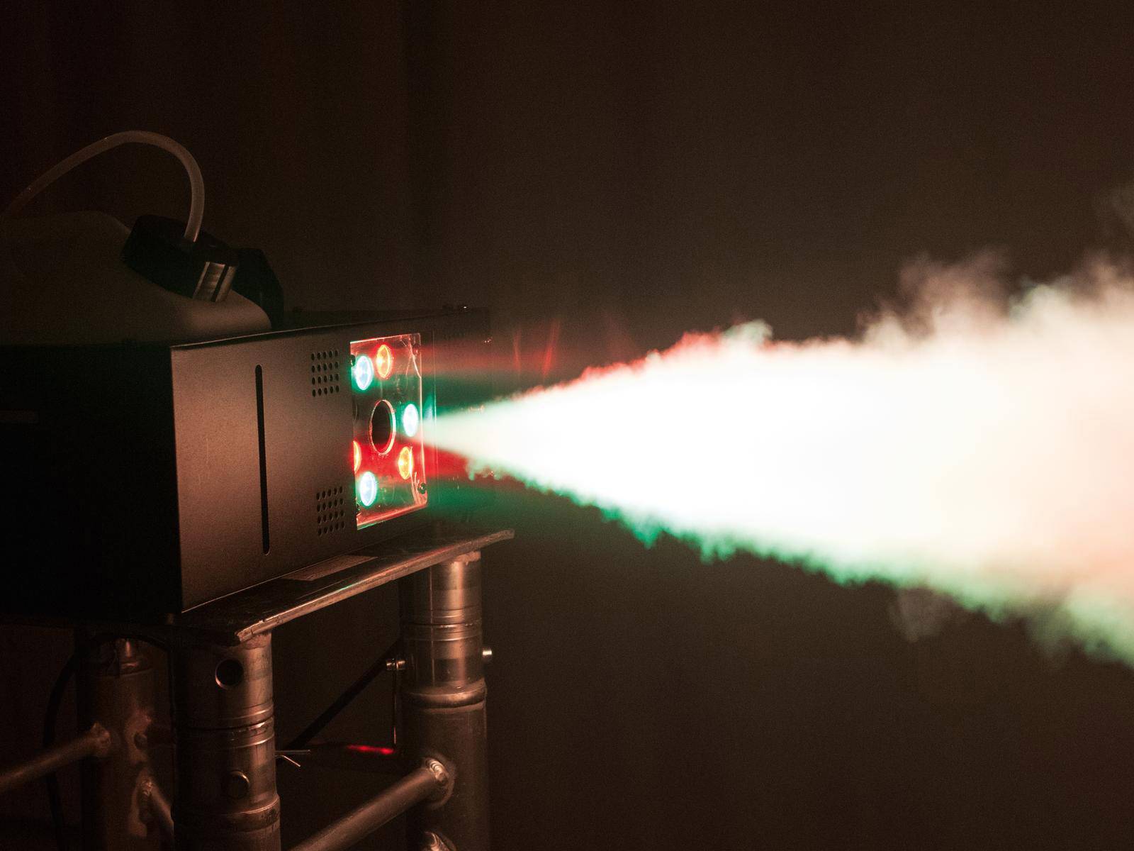 'Urządzenie zadymiające rzuca silny, kolorowy strumień światła przez mgłę, tworząc fascynujące efekty podczas występów scenicznych.'