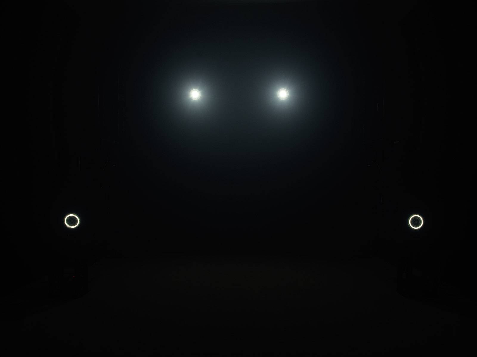 Ciemna przestrzeń z czterema świecącymi punktami: dwa na górze pośrodku, dwa na dole po bokach. Atmosfera tajemnicza i minimalistyczna.