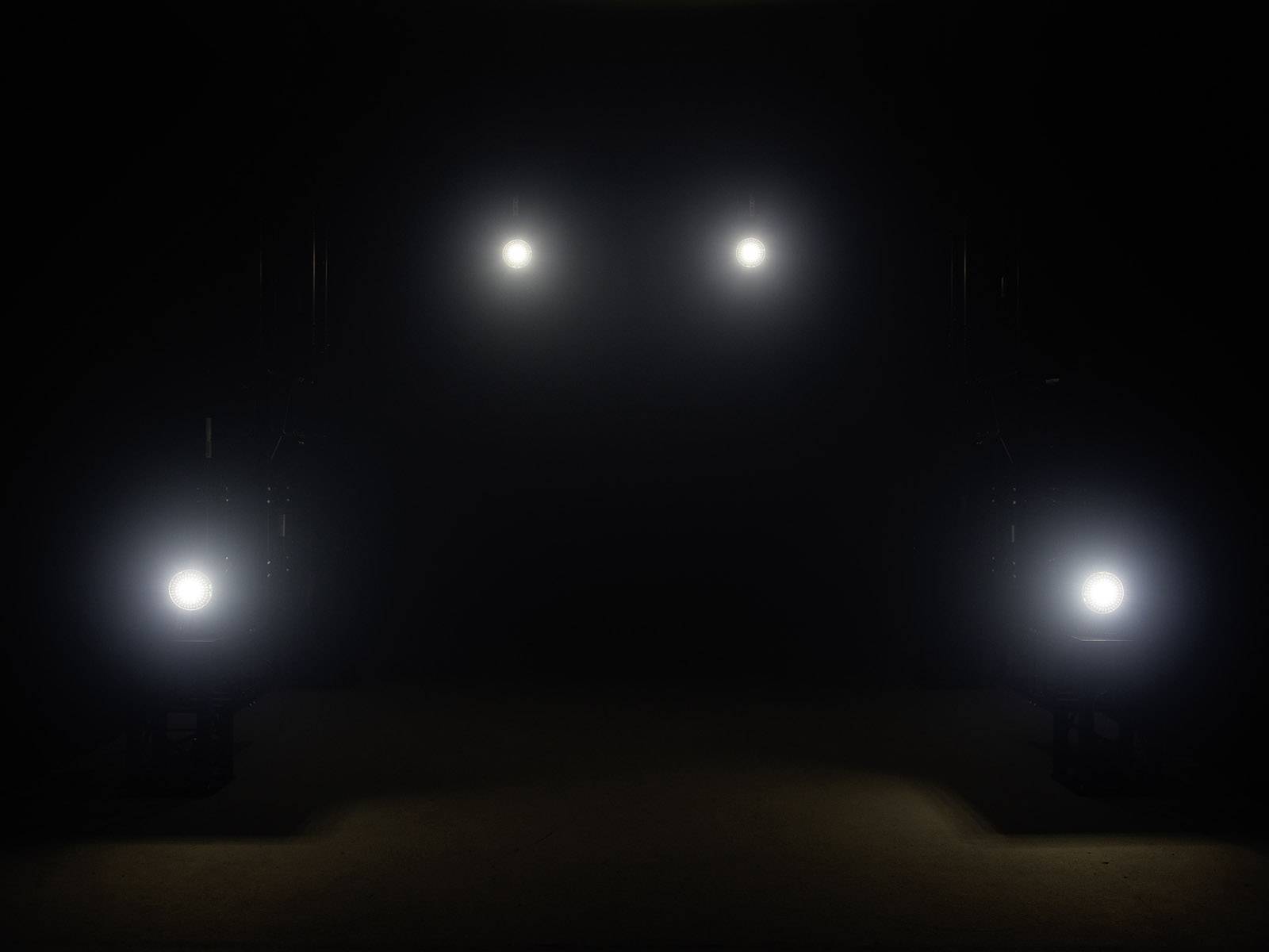 Cztery jasne światła świecą w ciemnym pomieszczeniu, rozmieszczone symetrycznie.