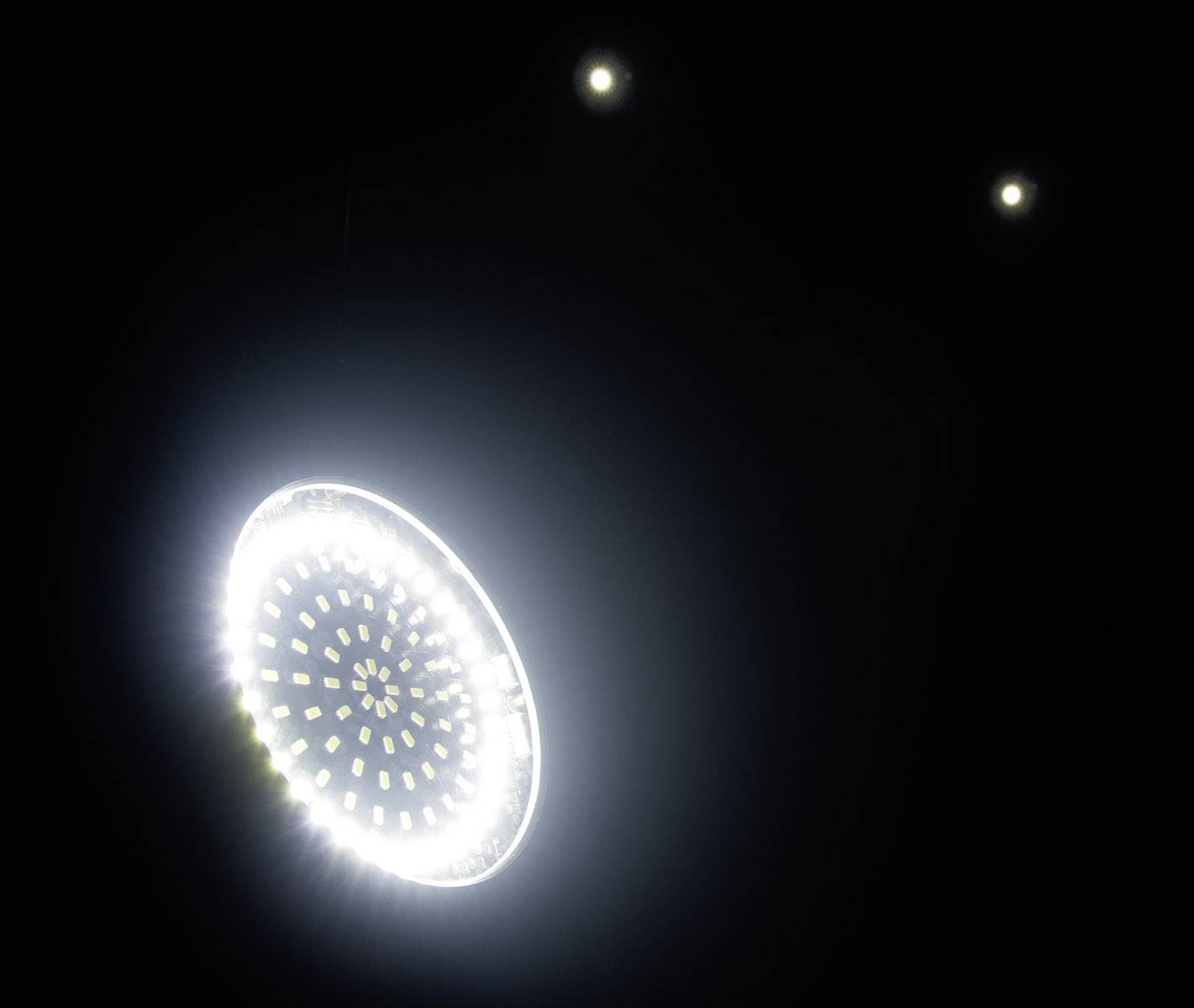 Świecący pierścień LED jarzy się w ciemnym otoczeniu, flanowany przez dwa małe, jasne punkty w tle.