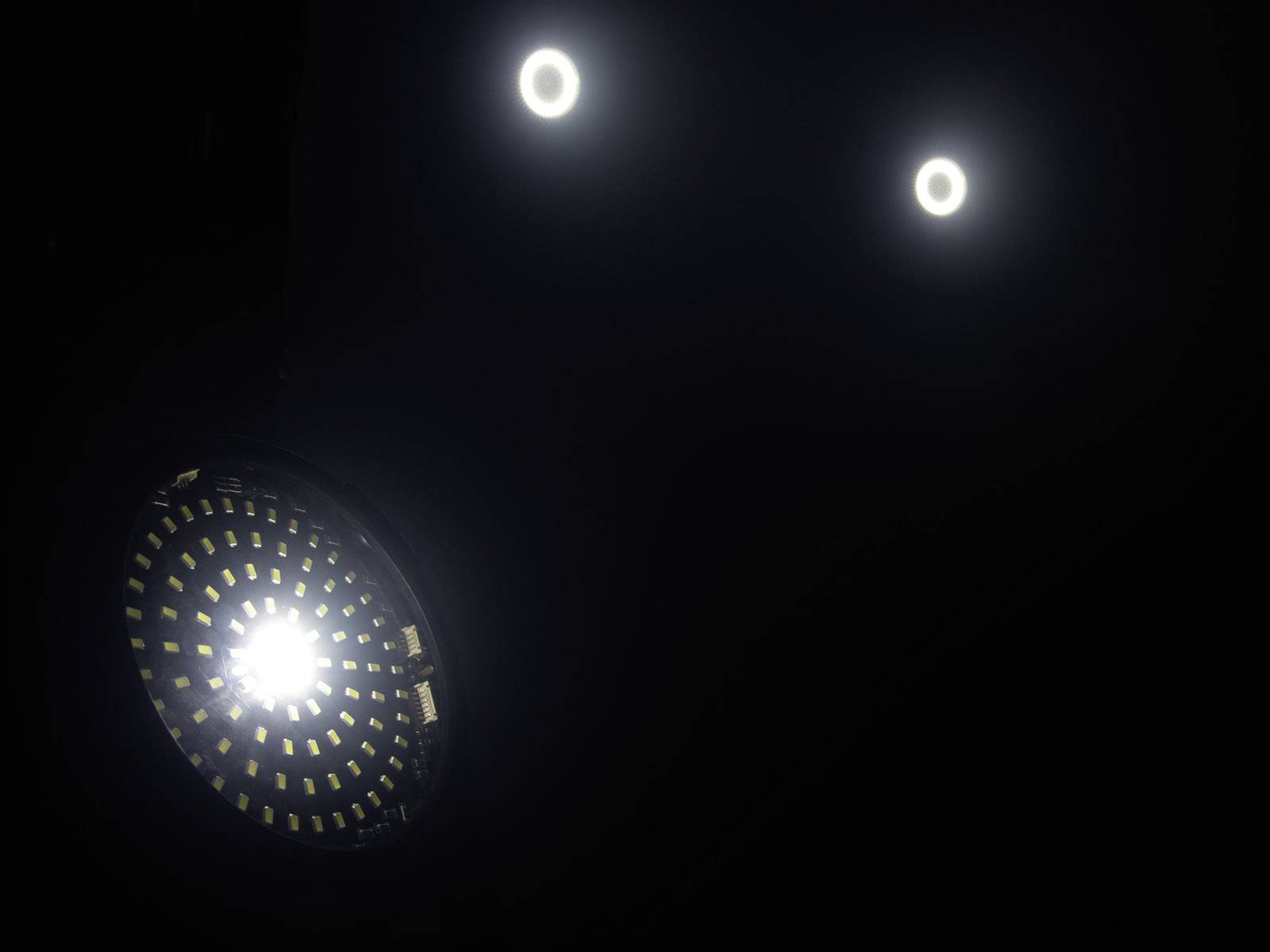 Trzy jaskrawe źródła światła w ciemnym pomieszczeniu, jeden z widocznymi diodami LED i dwa w formie okrągłych świetlnych pierścieni.