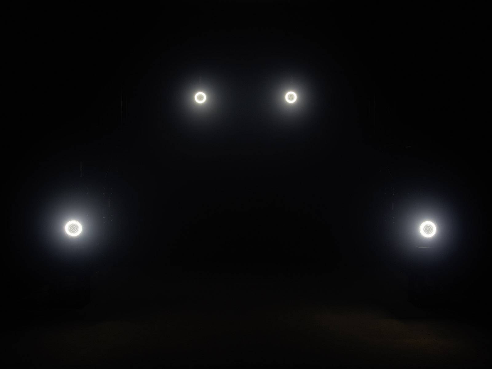 'Ciemne tło z czterema świecącymi reflektorami ustawionymi w parach, sugerujące zarys pojazdu.'