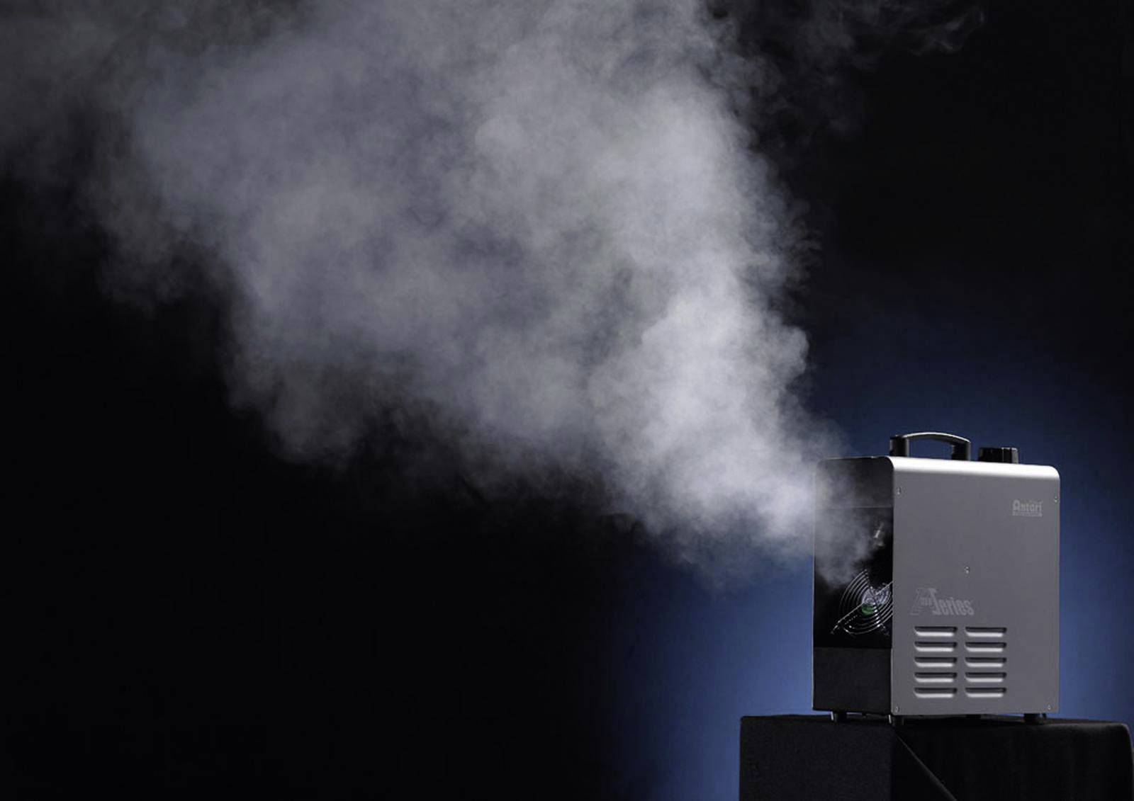 Maszyna mgielna w działaniu, wytwarza gęstą białą mgłę w ciemnym otoczeniu.