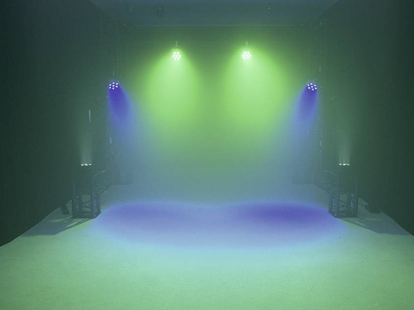 Zielone i niebieskie światło sceniczne pada na pustą płaszczyznę, otoczoną czarnym tłem.