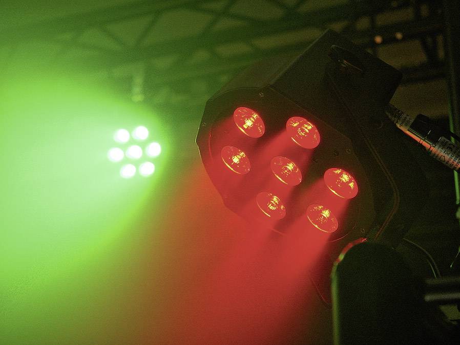 Reflektory sceniczne świecą na czerwono i zielono, rzucając kolorowe wiązki światła, które tworzą pełną nastroju atmosferę.