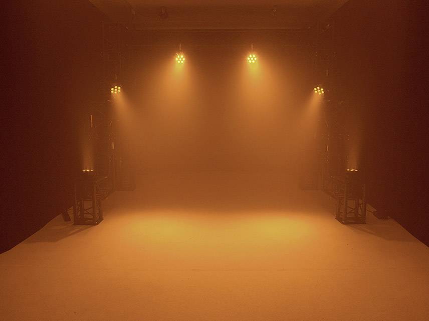 Pusta sala oświetlona pomarańczowym światłem, z wieloma reflektorami skierowanymi z góry i z boku na podłogę.