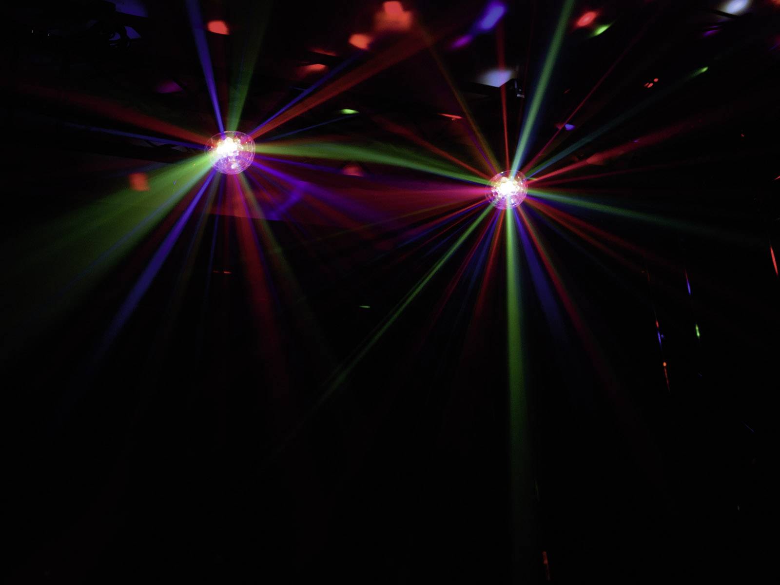 Dwie kule dyskotekowe rzucają kolorowe światła w ciemnym pomieszczeniu. Tworzą one żywy, świąteczny klimat.