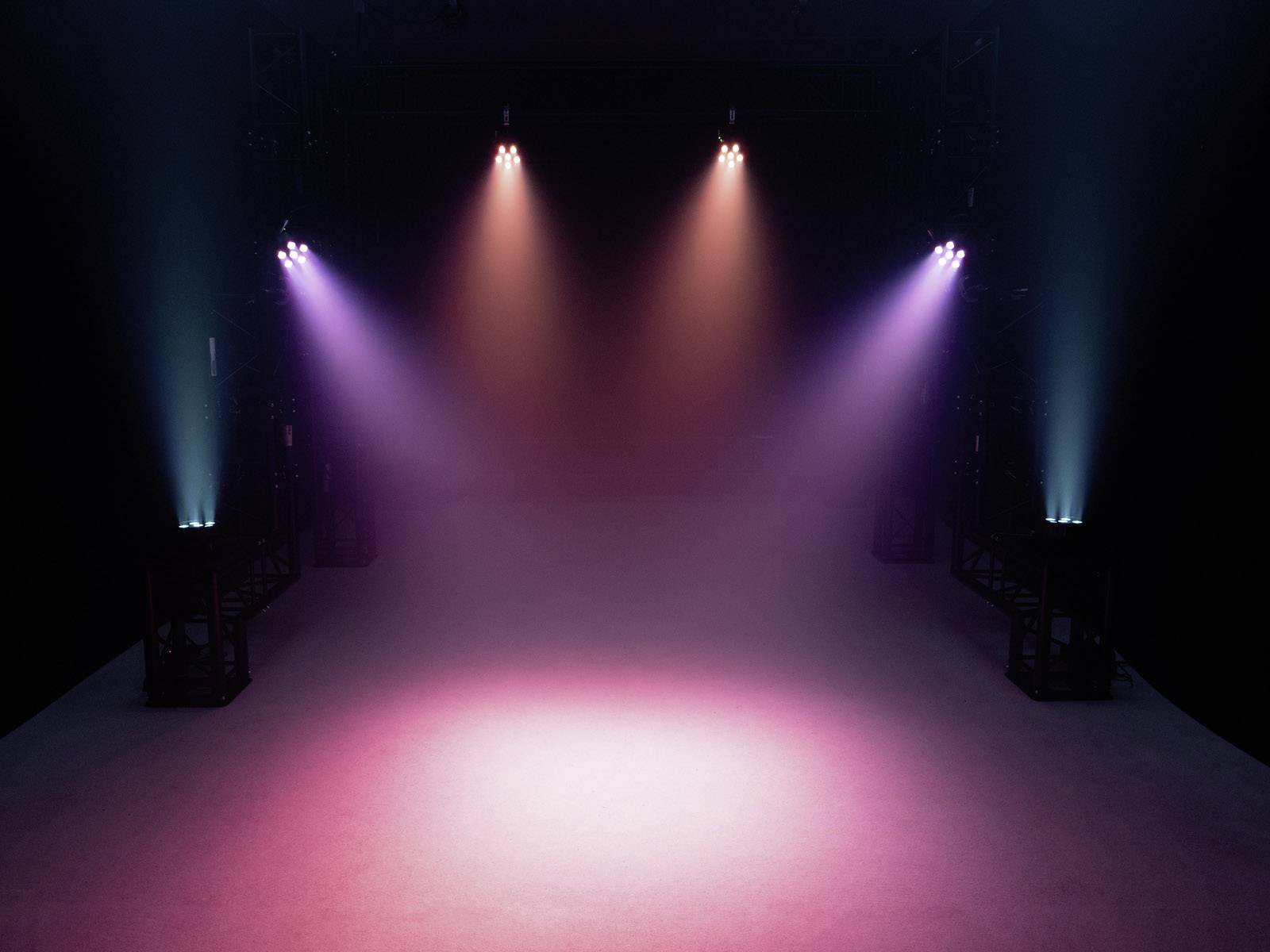 Scena z kolorowymi reflektorami, które świecą z góry i oświetlają pustą przestrzeń czerwonawym i fioletowym światłem.