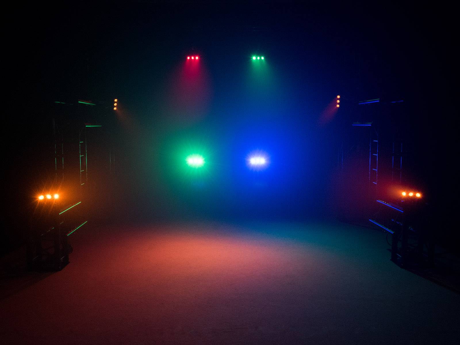 Ciemne pomieszczenie z kolorowymi światłami: czerwonymi, zielonymi i niebieskimi, które świecą z oświetlenia scenicznego w centrum.