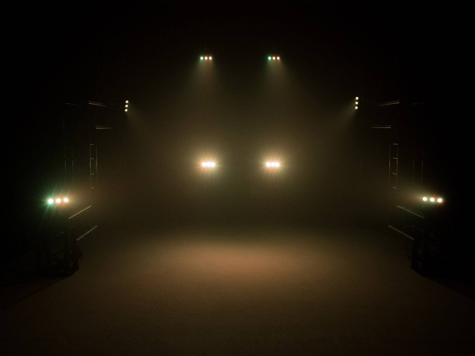 Kilka reflektorów oświetla ciemne pomieszczenie, rzucając wiązki światła do przodu.